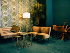 A bright teal living room with gold velvet couches and art deco wallpaper.