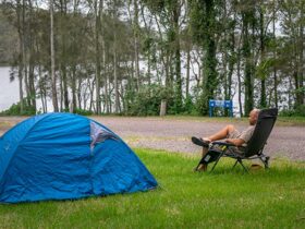 A man sitting by his tent at Violet Hill campground and picnic area in Myall Lakes National Park.