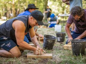 Men grinding stone to make a traditional Aboriginal axe head in a workshop