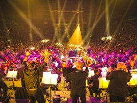 An orchestra performs to a crowd, with bright flashing lights overhead