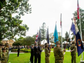 Anzac Day commemoration with flags and community members standing in the background