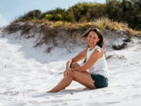 Laure is sitting side on wearing black shorts, white sleeveless t-shirt on white sand dune