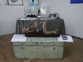 image shows artifacts from the Ice Pact exhibition including a skeleton crouching and paintings