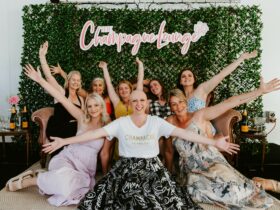8 women sat under The Champagne Lounge logo with their arms outstretched