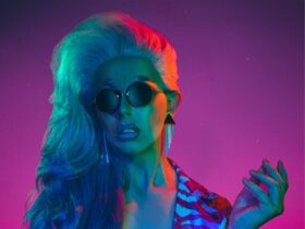 Drag queen Midas wearing sunglasses in front of a purple background
