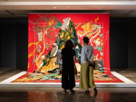 Two women from behind looking at a very large tapestry with Australian animals
