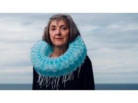 A photographic portrait of an older women with grey hair with a large blue necklace of face masks.