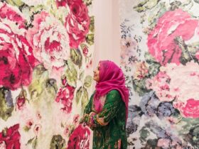 A person stands in a gallery space, flanked by large floral patterned artworks.