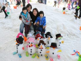 A family with 2 young children posing with the 8 snowmen they build.