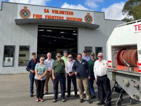 A group of museum volunteers stands in front of the Vehicle Pavilion with local MP