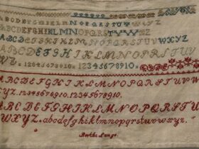 cross stitch sampler from 1800s with name Bertha Lange stitched in red.