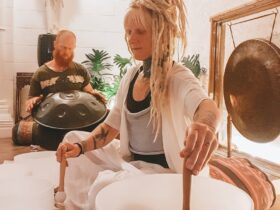 Woman playing crystal singing bowls with man in background playing handpan drum