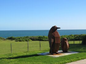 The rusty red penguins sit contemplating against a background of green land and blue sea and sky