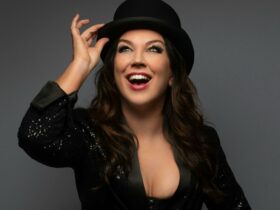 A performer in top hat and jacket is smiling and holding on to her hat