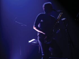 A saxophonist, veiled in darkness, with a blue light shining on him.