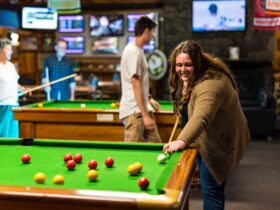 Young woman lining up a shot at one of the pool tables with a small group playing on table behind
