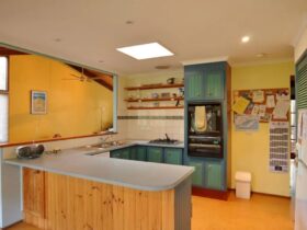 Image of old style kitchen with timber cabinets opening to living area