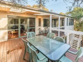 Image of large upstairs deck with outdoor table, outdoor kitchen and view to house indoors
