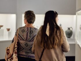An older and younger person side by side from behind, walking through an exhibition of artefacts
