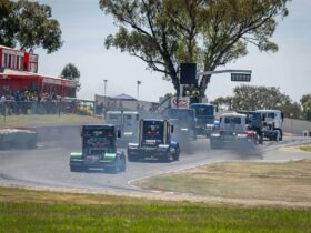 A grid of trucks racing up past spectators at Winton Motor Raceway