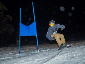man racing down snow hill at night snowboard