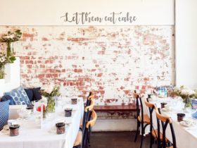 Exposed brick wall, with cursive 'Let them eat cake' written above. Two tables set for high tea.