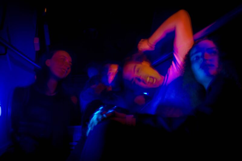 A group of teenagers sit around on a staircase in intense nightclub light.