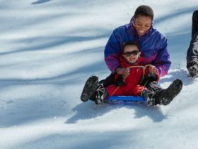 A mother and son riding a toboggan down a slope covered in snow, with big smiles on their faces.