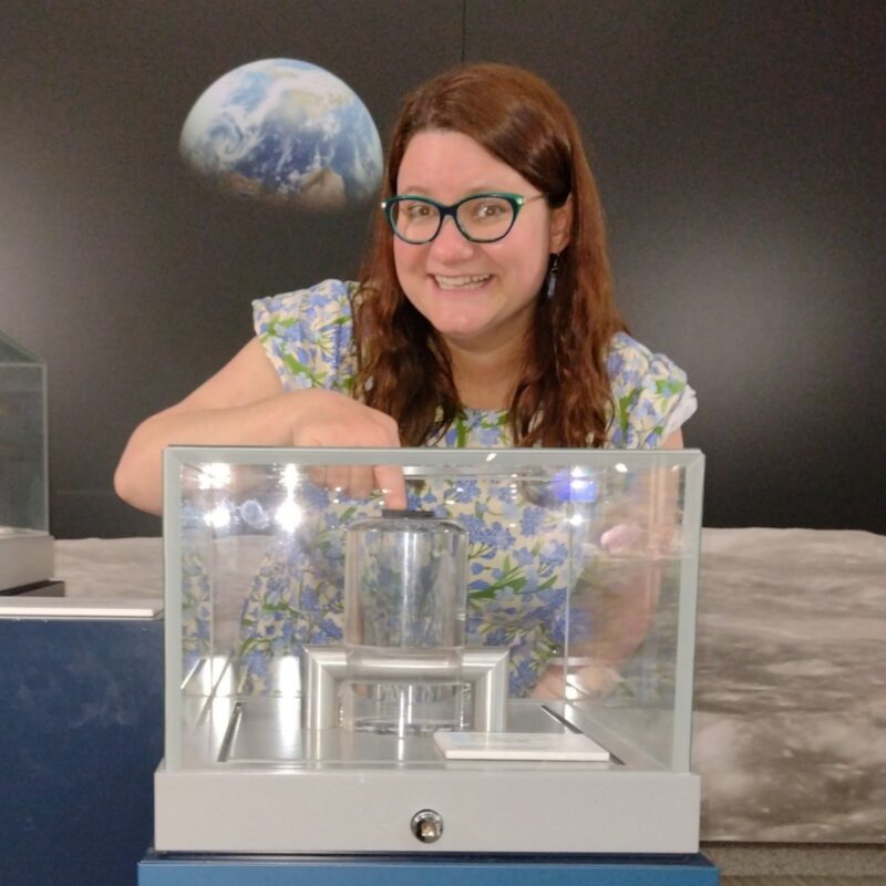 A woman touches a small rock in a cabinet with an image of the Moon and Earth behind her.
