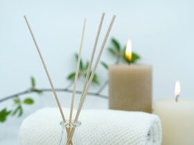 Reed diffuser, towel and lit candles against a white backdrop.