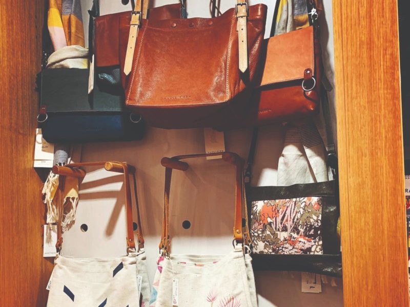 Leather handbags hanging on a pegboard display with printed linen totes