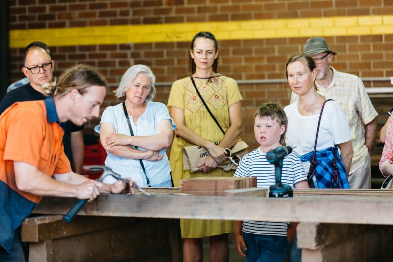 Visitors of all ages enjoying a demonstration by skilled craftsman and staff member