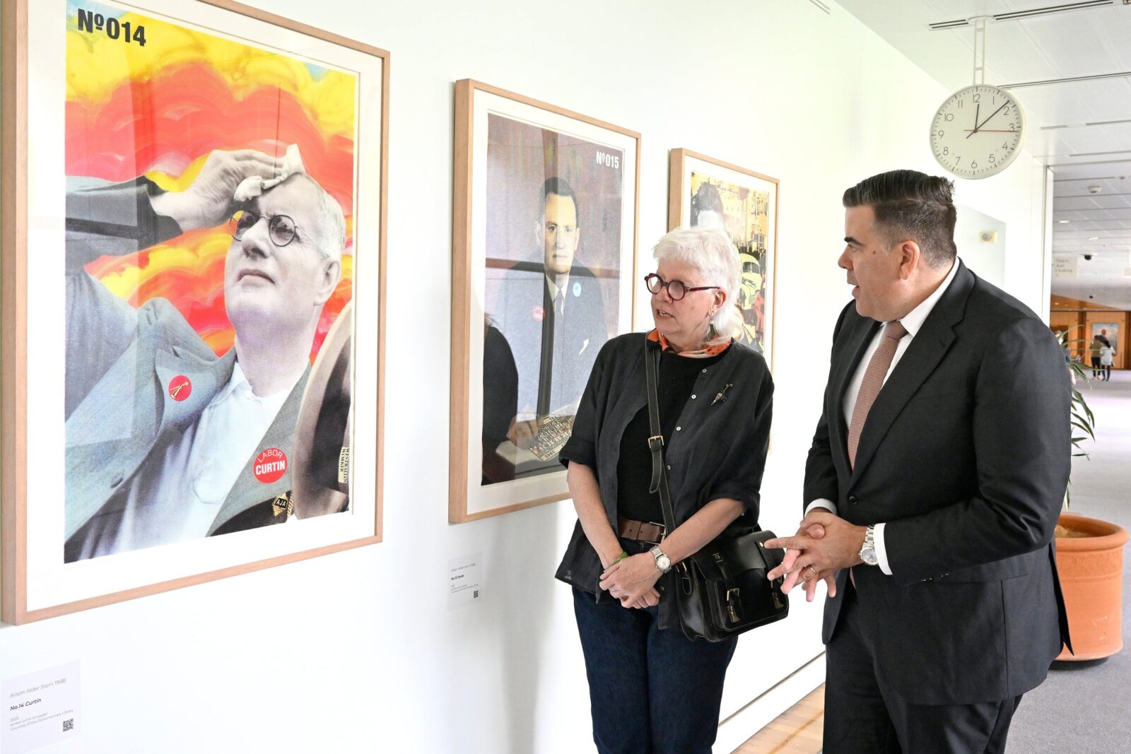A man and woman looking at art work hanging on a wall and having a conversation.