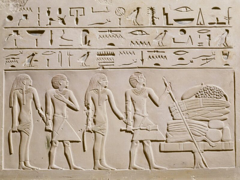 Deatil of a rectangular stone with three rows of hieroglyphics carved at the top and four figures