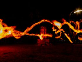 A long exposure photo of fire twirlers, with lines of flames pictured across a dark night background
