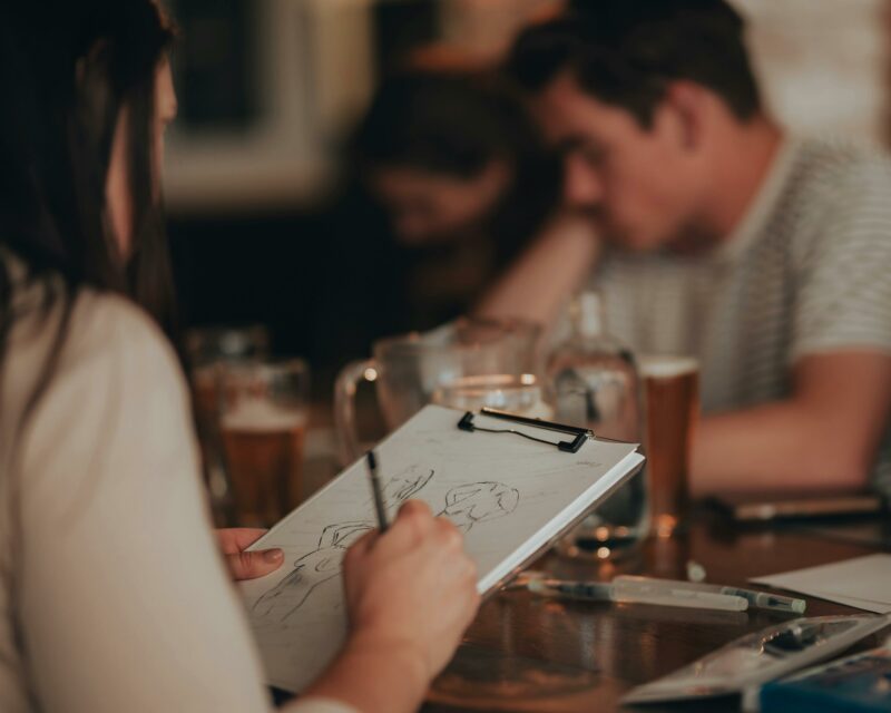 Person drawing in foreground, with glasses of beer on table