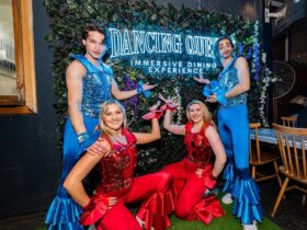 Performers posing in front of neon dancing queen dining experience sign