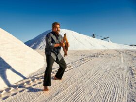 man standing amongst sand dunes holding two boomerangs