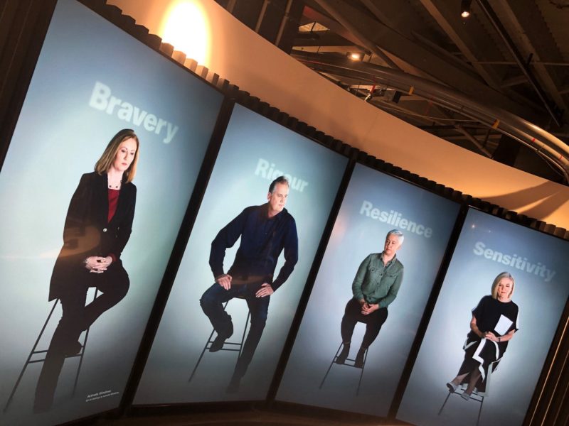 Four 7-foot tall video screens showing four journalists sitting on stools