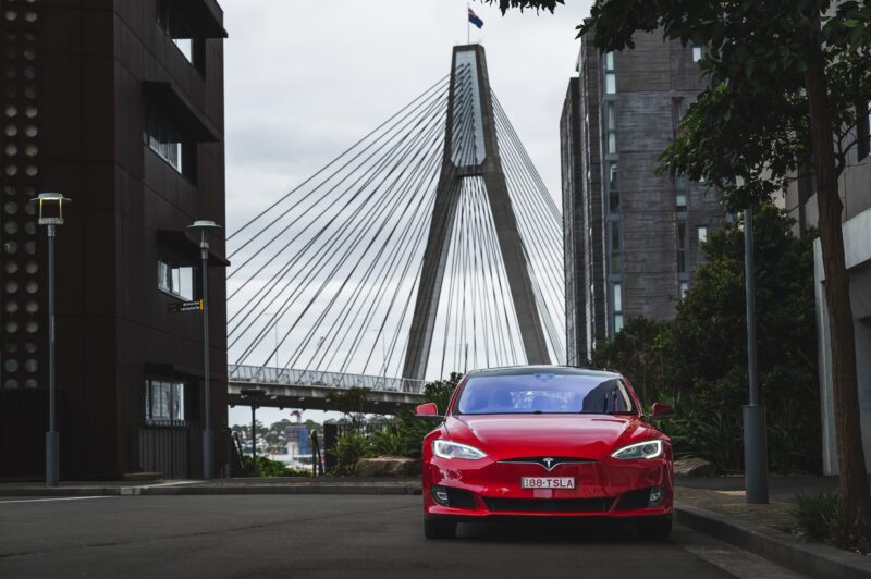 a red tesla parked with a bridge and city background waiting to be hired