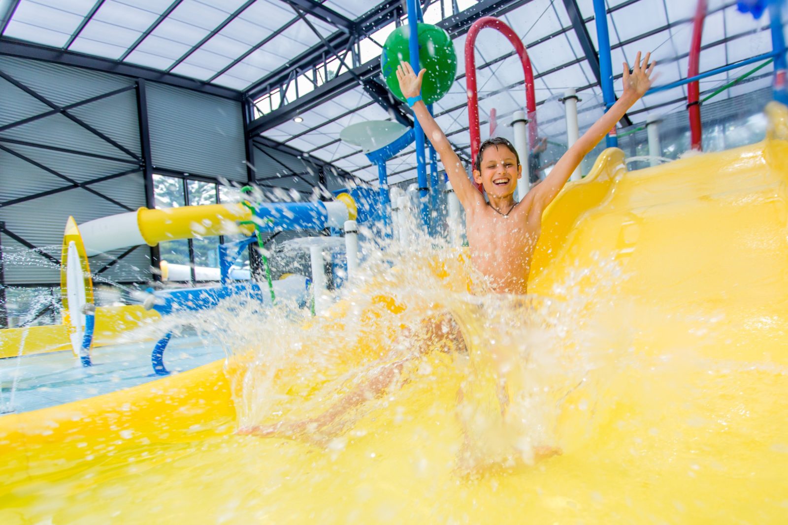 Boy sliding down indoor heated water slide. Water going everywhere, boy having so much fun!