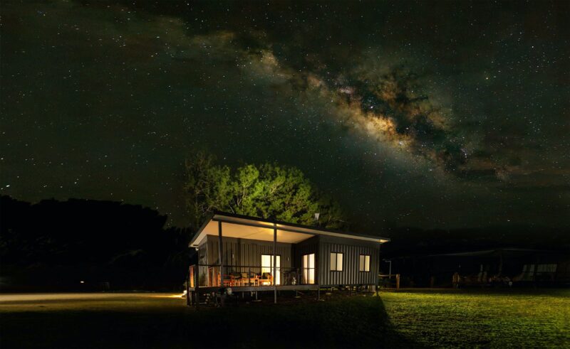An image of Wollumbin cottage sitting in a paddock at night with the Milky Way arching over the top.