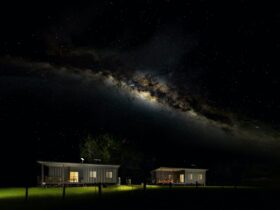 An image of both cottages sitting in a paddock at night with the Milky Way arching over the top.