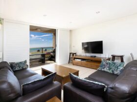 Lounge room with lounges, TV and ocean views, leading out to furnished balcony