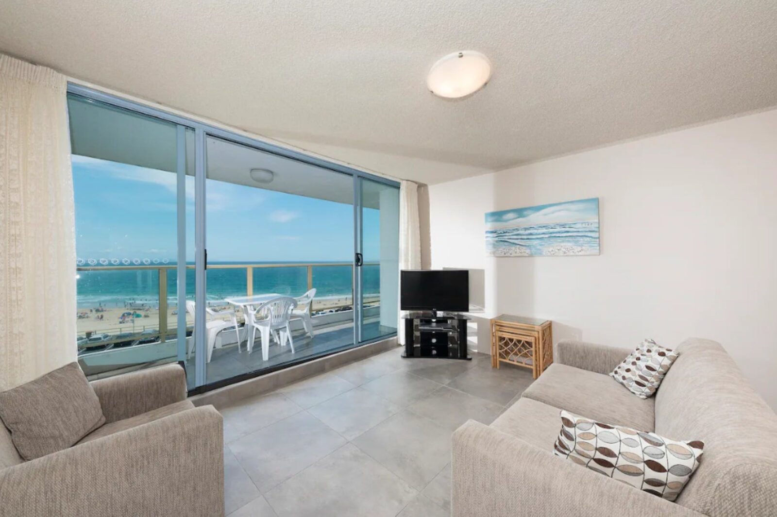 Loungeroom with lounges, TV, leading out to balcony with uninterrupted beach views, casual setting