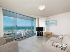 Loungeroom with lounges, TV, leading out to balcony with uninterrupted beach views, casual setting