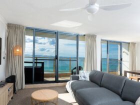 Lounge room with TV, lounges, looking out to balcony with setting and stunning beach views