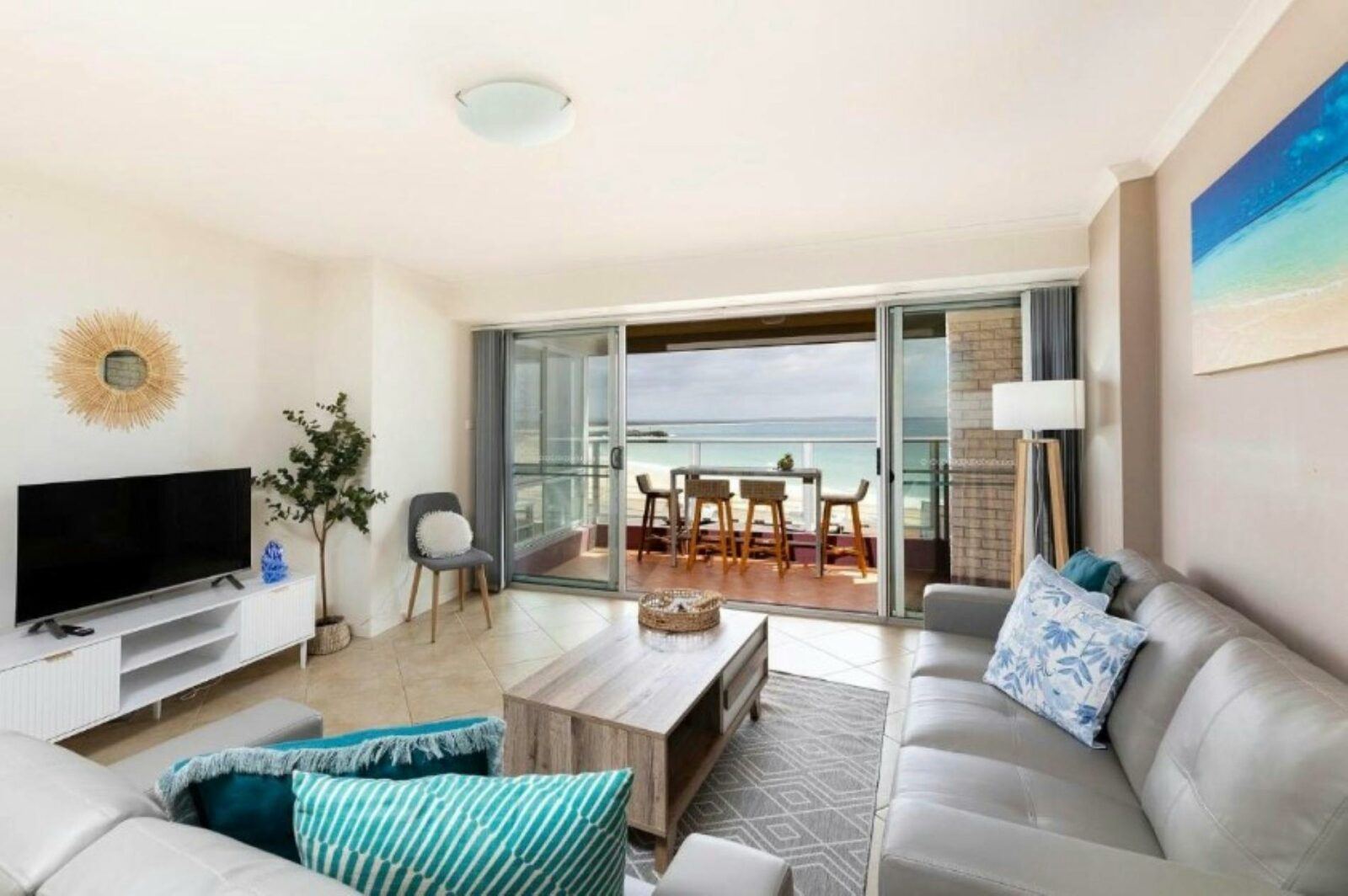 Loungeroom with lounges, TV, leading out to balcony with uninterrupted beach views, high bar setting