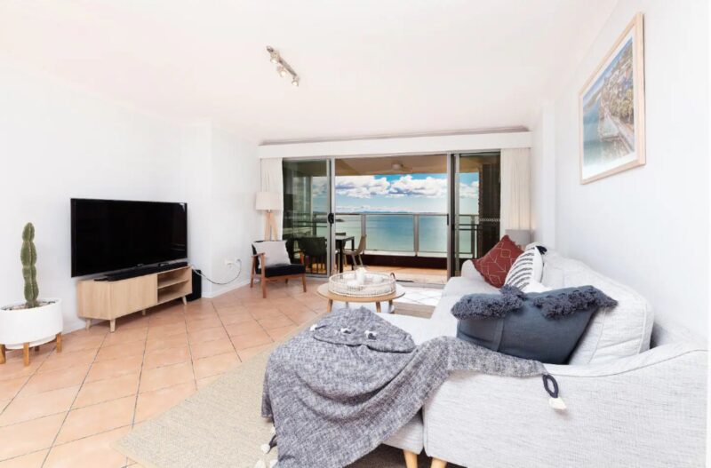 Loungeroom with spacious lounges, TV, out to balcony with 4 seater setting and stunning beach views