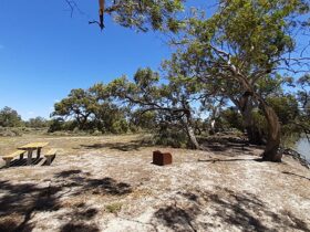 A picnic table and wood barbecue on the banks of the river at Lachlan River campground in Kalyarr